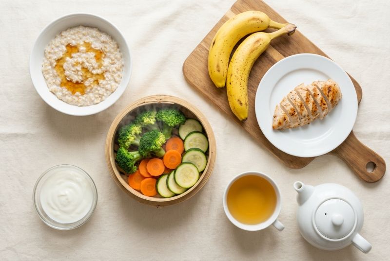 오트밀, 찐 채소, 바나나, 닭가슴살, 요구르트, 허브차 등 위염에 좋은 음식이 차려진 식탁을 위에서 내려다 본 사진